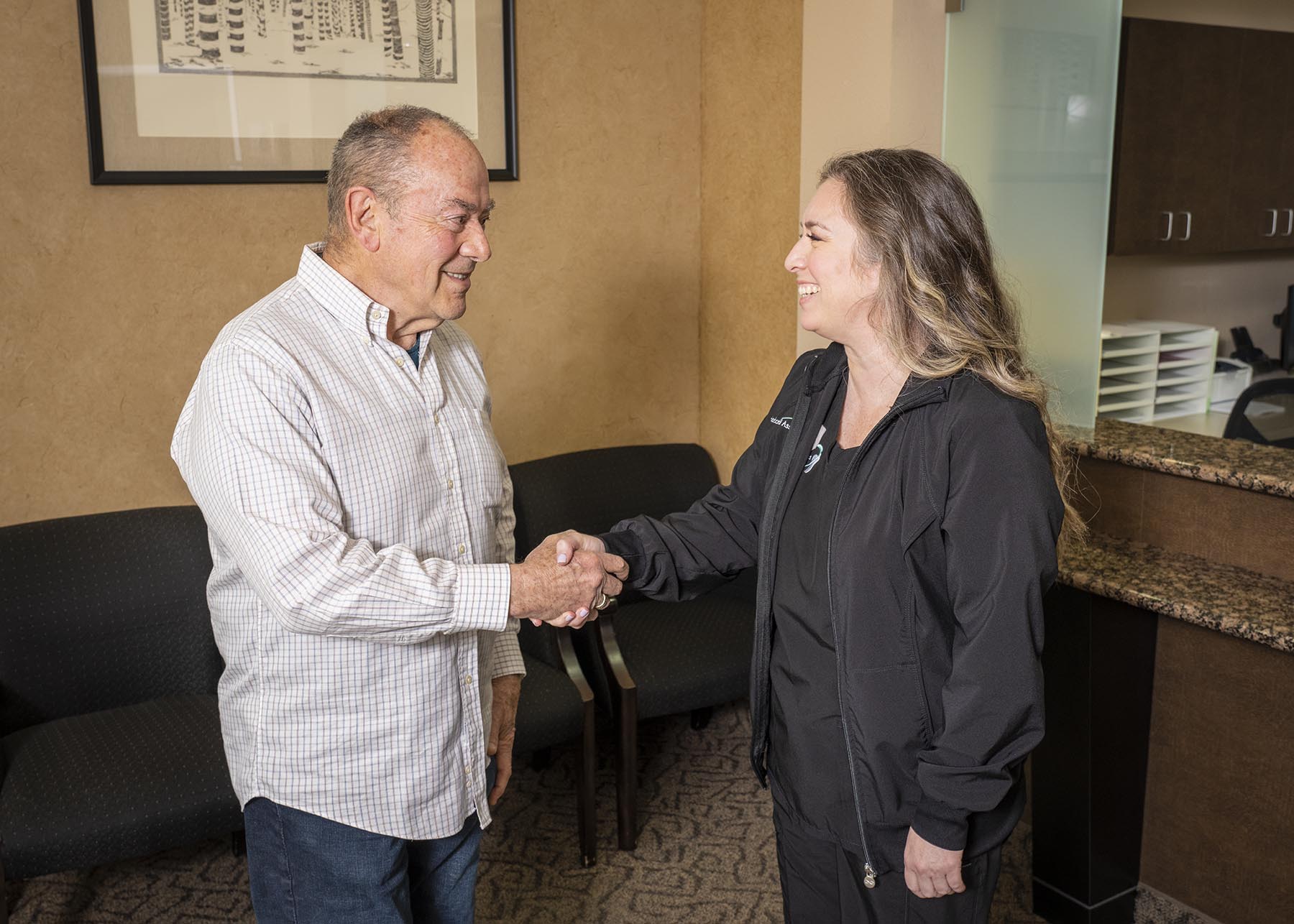 A dental assistant and a patient shaking hands