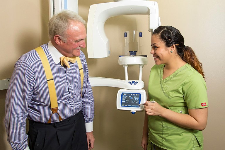 An image of a patient being shown the digital X-ray machine by a dental assistant.