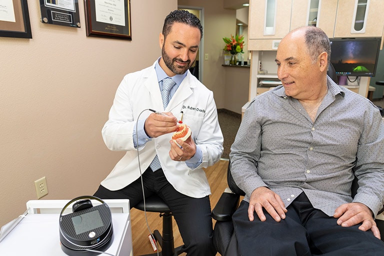 An image of Dr. Ovadia holding a model of teeth and showing a patient how the dental laser is a minimally invasive treatment.